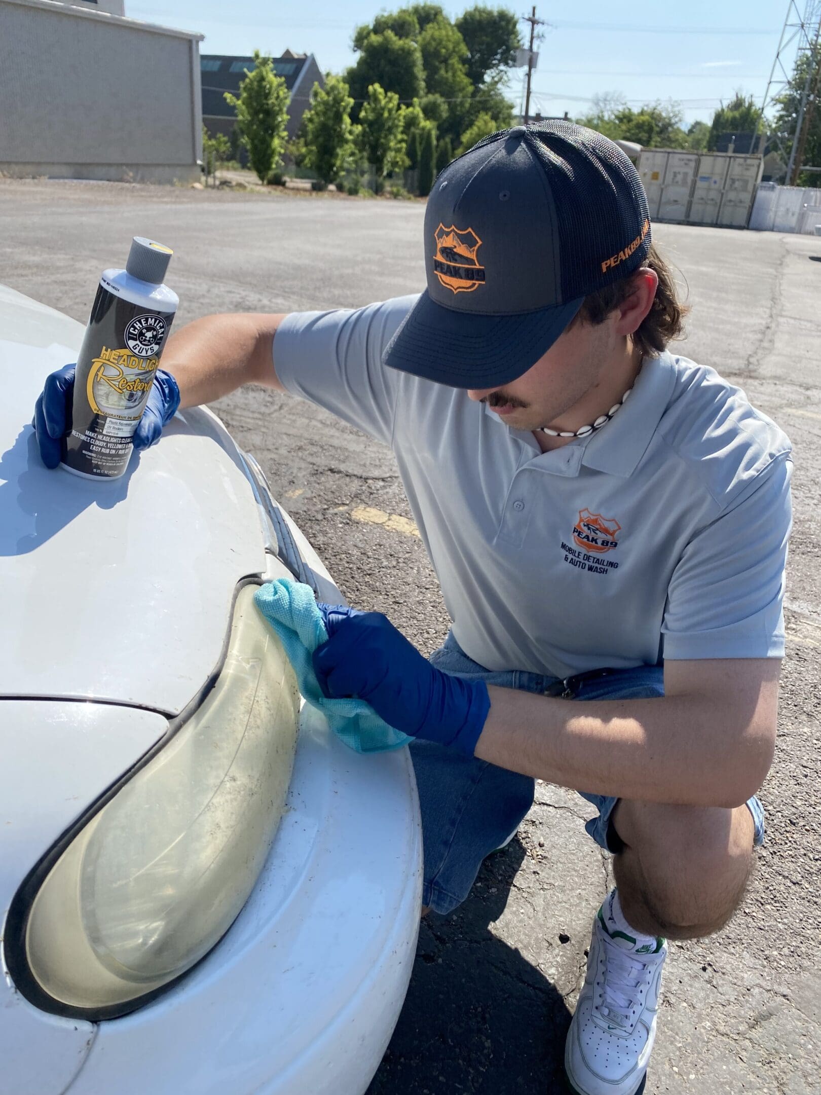 A man in blue gloves is cleaning the hood of his car.